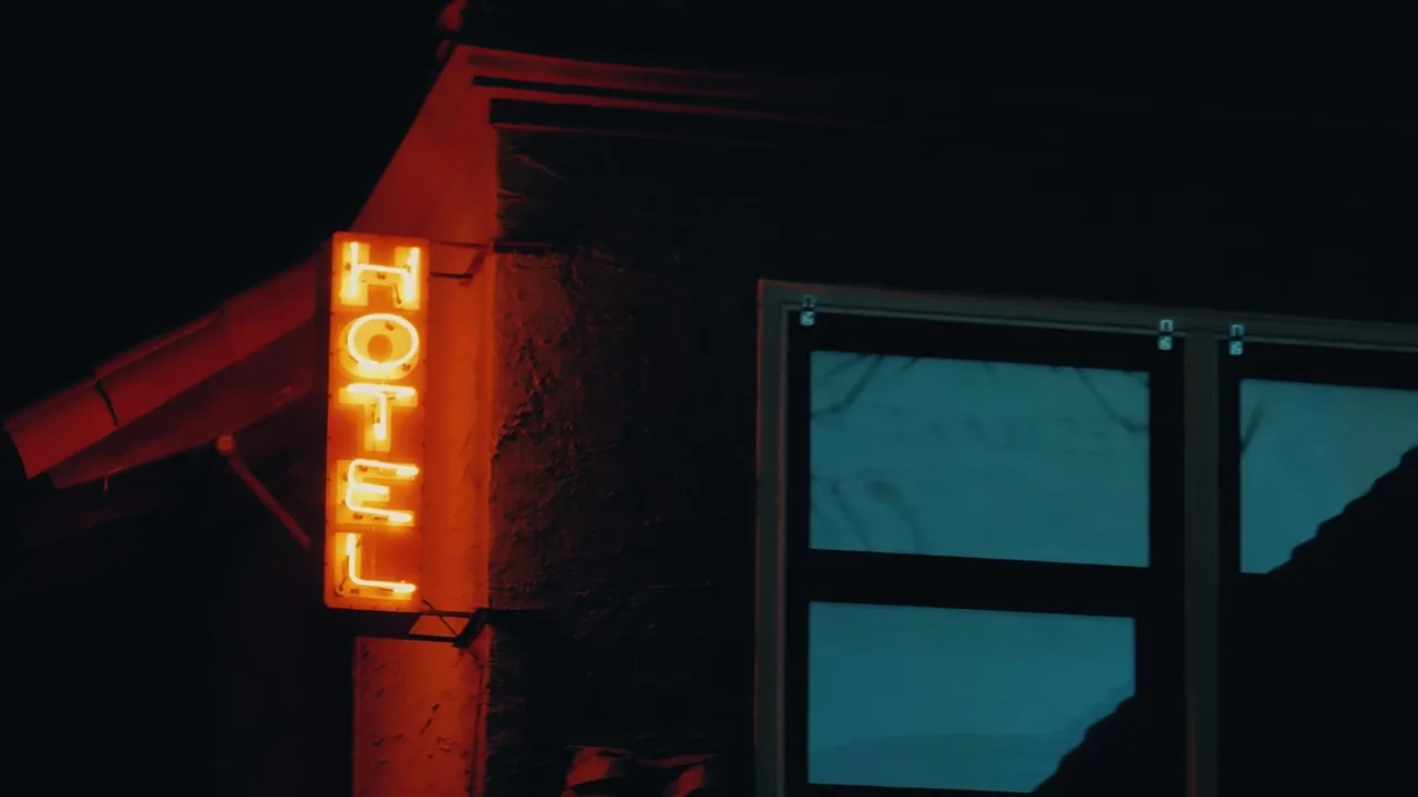Red neon hotel sign beside teal windows at night